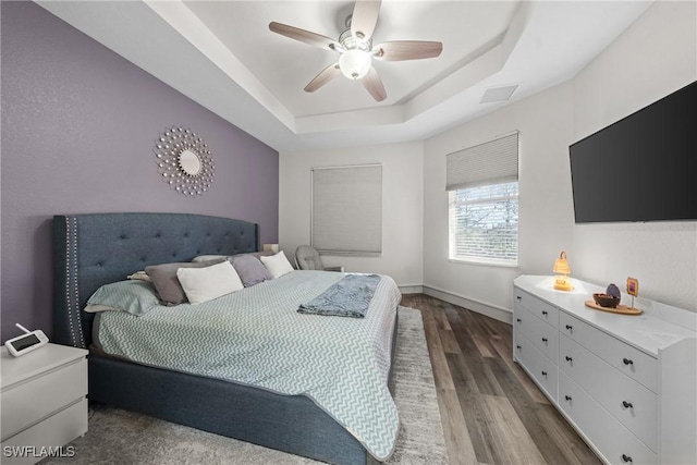 bedroom featuring a tray ceiling, visible vents, a ceiling fan, wood finished floors, and baseboards