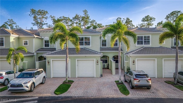 multi unit property with a garage, driveway, a tile roof, and stucco siding