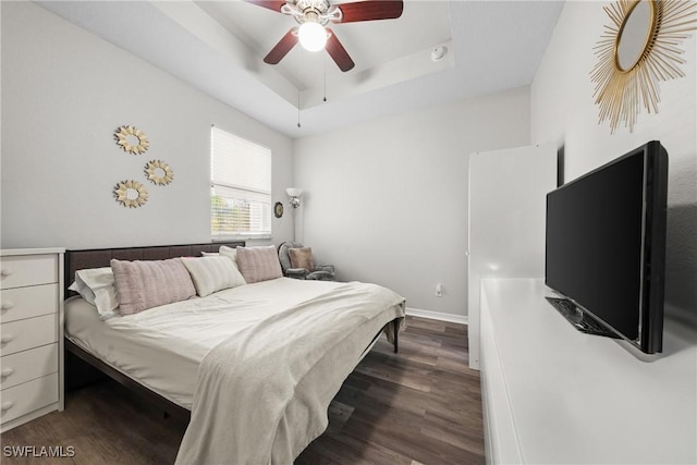 bedroom featuring a tray ceiling, ceiling fan, baseboards, and wood finished floors