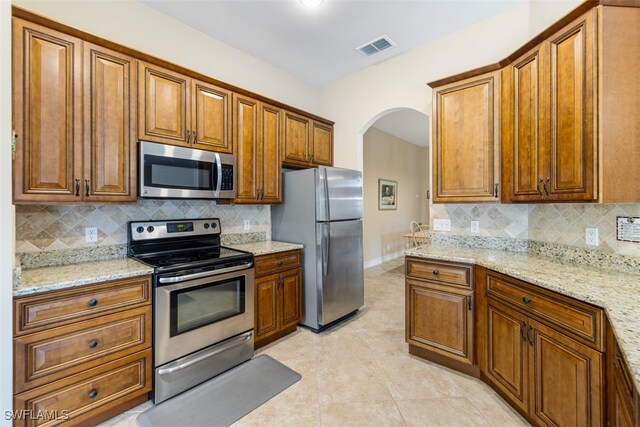 kitchen featuring arched walkways, stainless steel appliances, visible vents, and brown cabinets