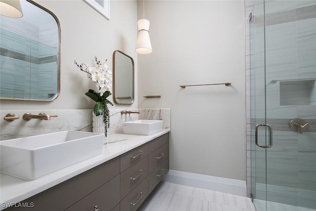 bathroom with double vanity, a stall shower, baseboards, and a sink