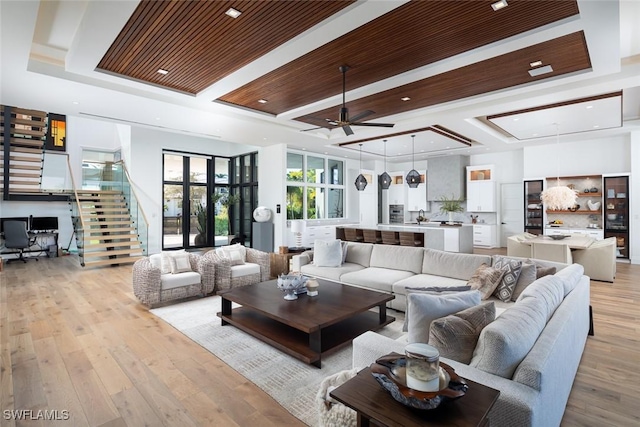 living room with light wood finished floors, ceiling fan, stairway, wood ceiling, and a tray ceiling