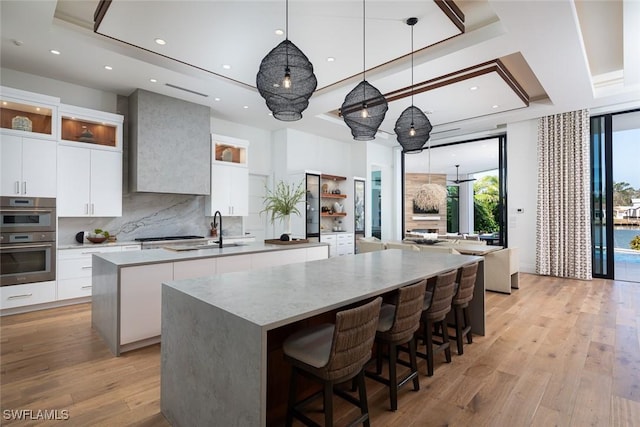 kitchen featuring light wood-type flooring, a large island, modern cabinets, a tray ceiling, and double oven