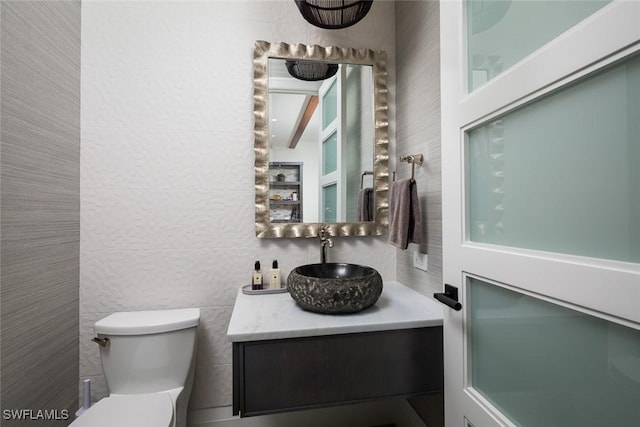 bathroom with toilet, vanity, and tile walls