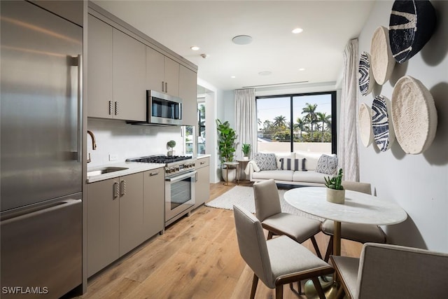 kitchen featuring high quality appliances, gray cabinets, light wood finished floors, and a sink