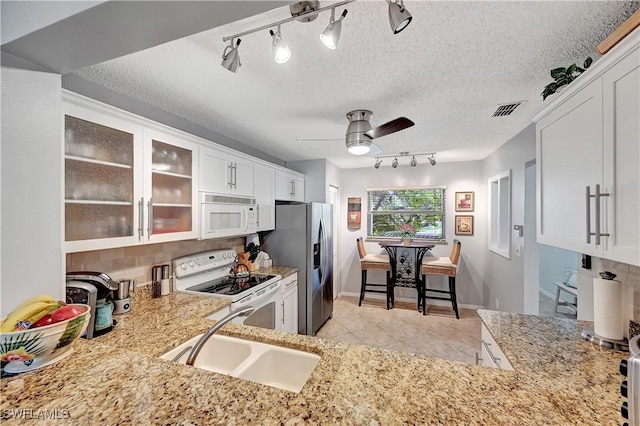 kitchen with white appliances, a sink, visible vents, white cabinets, and glass insert cabinets