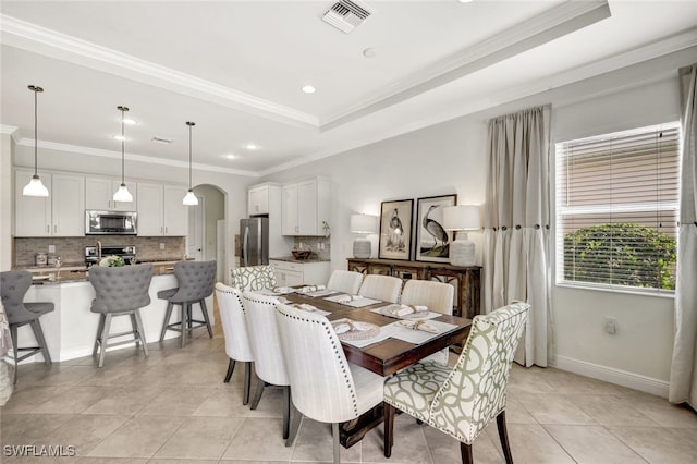 dining area with light tile patterned floors, visible vents, arched walkways, a tray ceiling, and crown molding