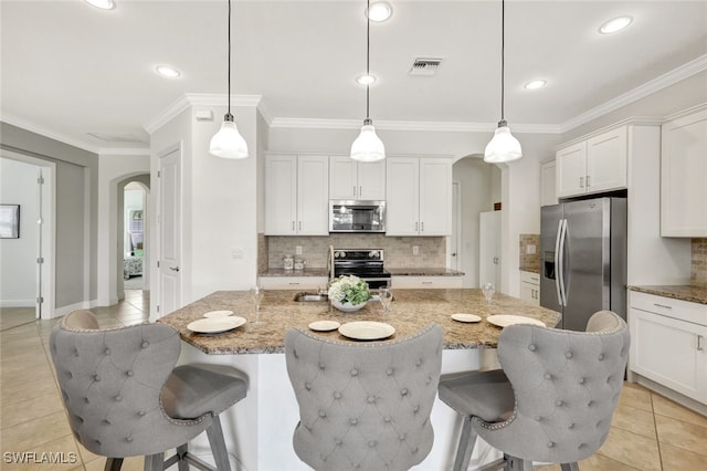 kitchen featuring appliances with stainless steel finishes, arched walkways, decorative light fixtures, and a kitchen island with sink