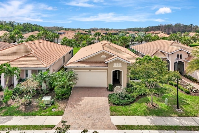 mediterranean / spanish house with a garage, decorative driveway, a tile roof, and stucco siding