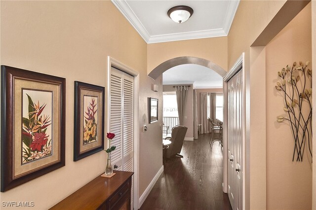 hallway with baseboards, arched walkways, dark wood-type flooring, and crown molding