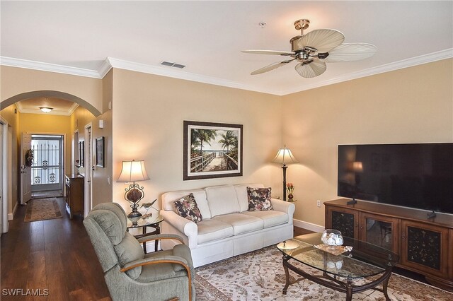 living room featuring arched walkways, visible vents, a ceiling fan, ornamental molding, and dark wood finished floors