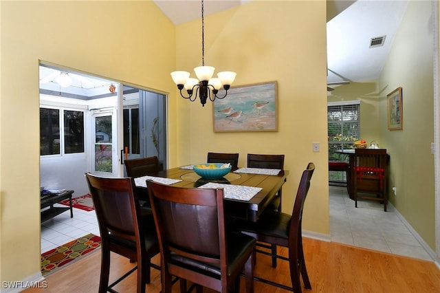 dining space with high vaulted ceiling, a notable chandelier, visible vents, baseboards, and light wood finished floors