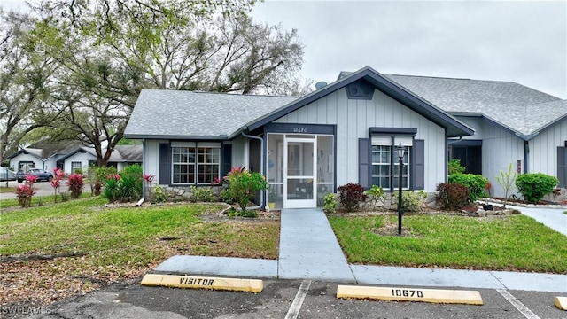 view of front of property featuring a shingled roof, uncovered parking, a front lawn, and board and batten siding