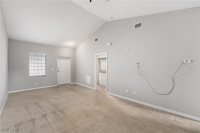 empty room with high vaulted ceiling, light colored carpet, visible vents, and baseboards