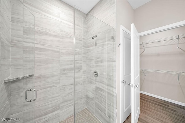 bathroom with a shower stall, a spacious closet, baseboards, and wood finished floors