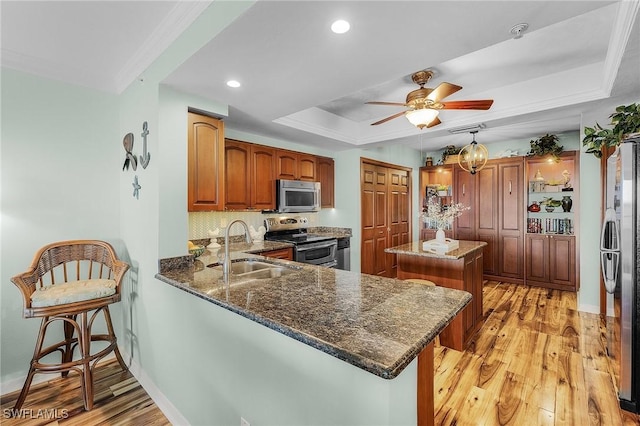 kitchen with a raised ceiling, appliances with stainless steel finishes, brown cabinets, a peninsula, and a sink