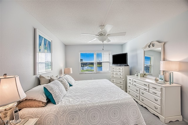 bedroom featuring light carpet, ceiling fan, and a textured ceiling