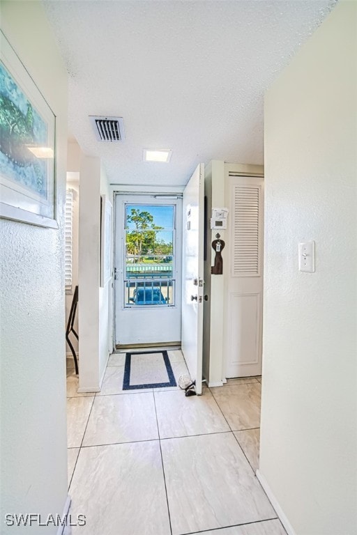 doorway to outside with baseboards, visible vents, a textured ceiling, and light tile patterned flooring