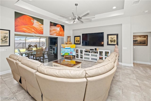 living room featuring a ceiling fan, a raised ceiling, visible vents, and baseboards