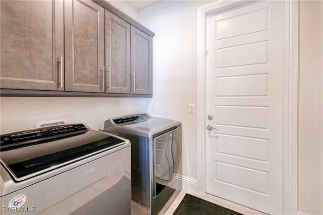 clothes washing area featuring baseboards, cabinet space, and washing machine and clothes dryer