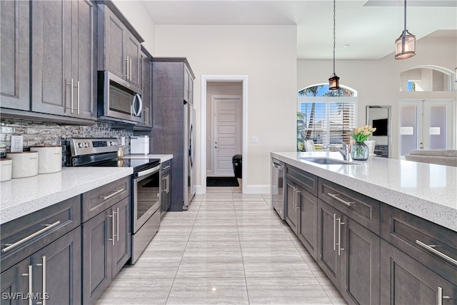 kitchen featuring dark brown cabinetry, hanging light fixtures, light stone countertops, stainless steel appliances, and a sink