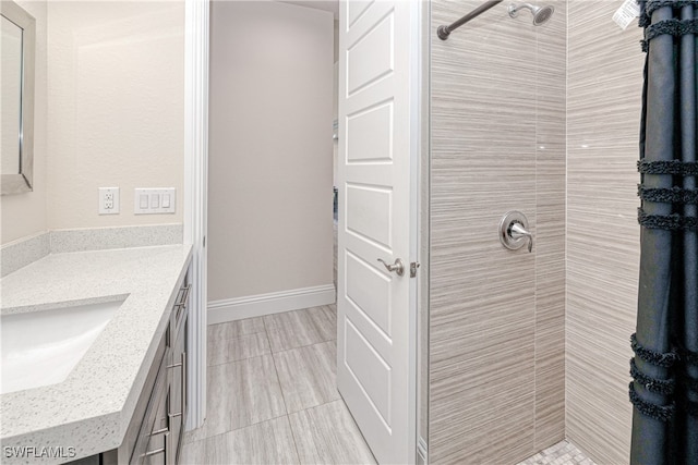 full bathroom featuring baseboards, tiled shower, and vanity