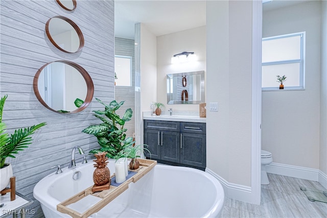 bathroom featuring a wealth of natural light, a soaking tub, vanity, and toilet