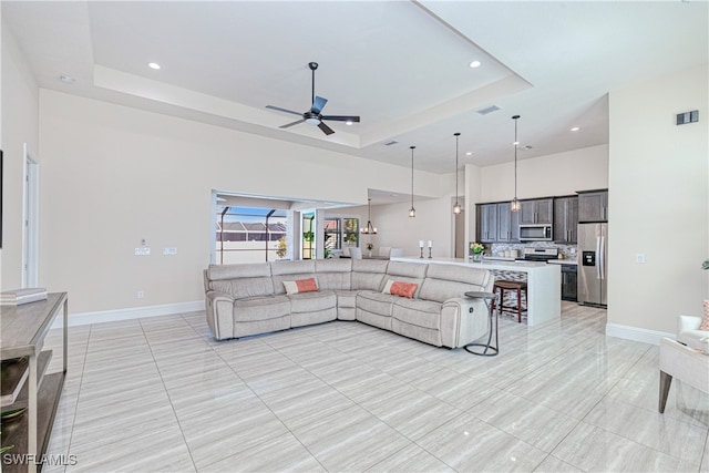 living area with a towering ceiling, visible vents, a tray ceiling, and baseboards