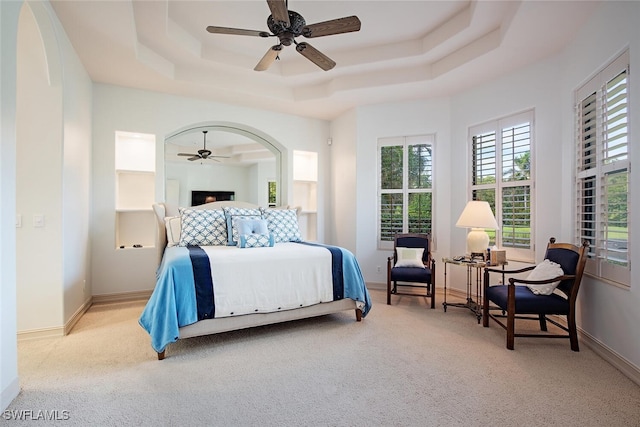 bedroom with light carpet, a tray ceiling, and baseboards