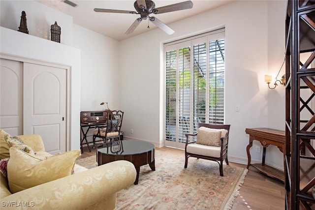 living room featuring ceiling fan, visible vents, light wood-style flooring, and baseboards