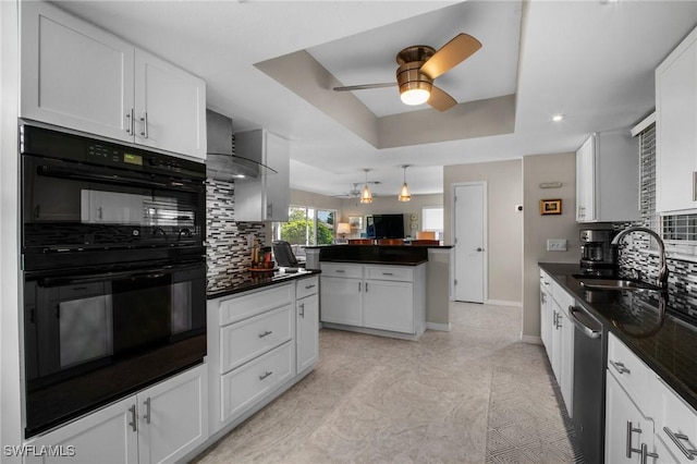 kitchen with dobule oven black, dark countertops, wall chimney exhaust hood, a tray ceiling, and white cabinetry