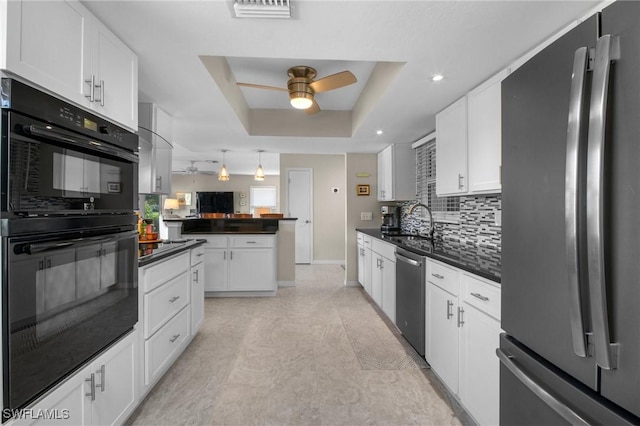 kitchen with tasteful backsplash, white cabinets, a raised ceiling, dark countertops, and stainless steel appliances