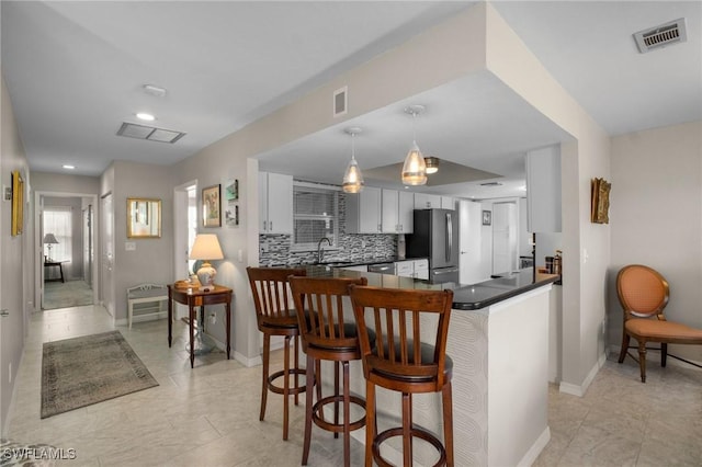 kitchen featuring visible vents, dark countertops, a kitchen breakfast bar, freestanding refrigerator, and a peninsula