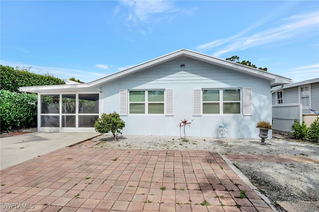 rear view of property with a sunroom, driveway, a patio, and stucco siding