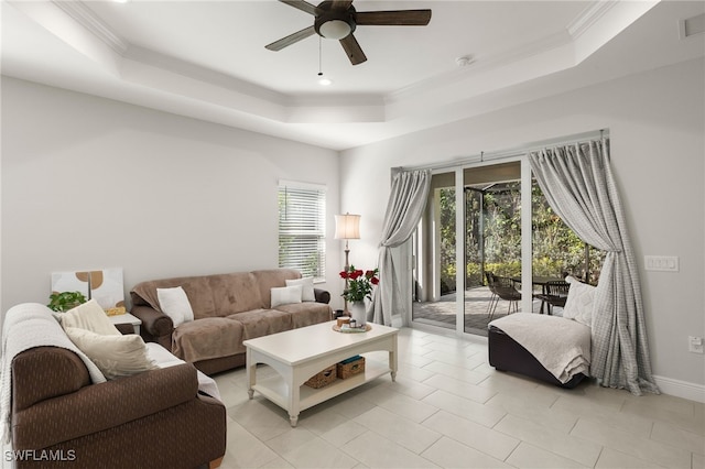 living area with light tile patterned floors, baseboards, ceiling fan, ornamental molding, and a tray ceiling