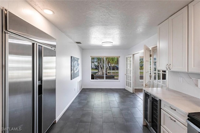 kitchen with a textured ceiling, wine cooler, built in refrigerator, white cabinets, and light countertops