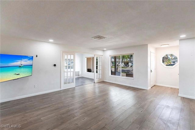 unfurnished living room with french doors, visible vents, baseboards, and wood finished floors