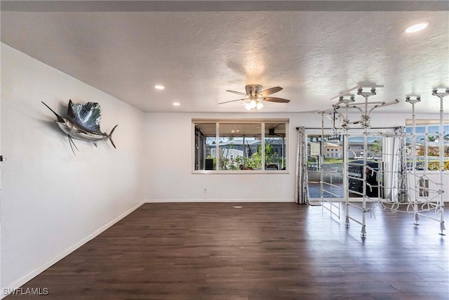 unfurnished room with ceiling fan, a textured ceiling, baseboards, and dark wood-type flooring