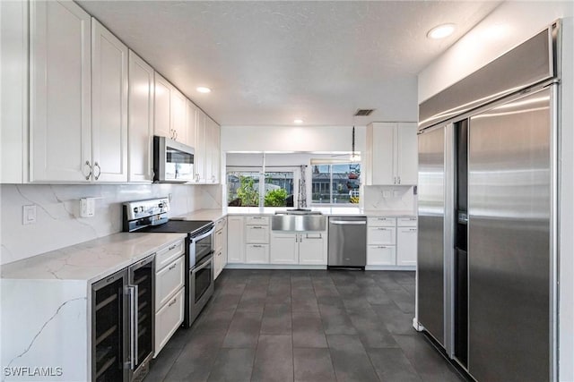 kitchen with light stone counters, wine cooler, stainless steel appliances, a sink, and white cabinetry