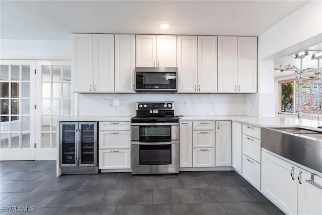 kitchen with appliances with stainless steel finishes, wine cooler, light countertops, and white cabinetry