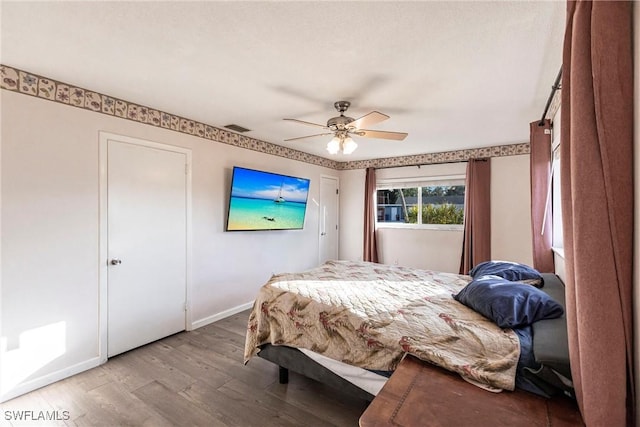 bedroom featuring a ceiling fan, visible vents, baseboards, and wood finished floors