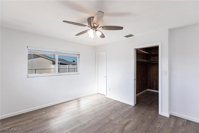 unfurnished bedroom featuring wood finished floors, visible vents, baseboards, a spacious closet, and a closet