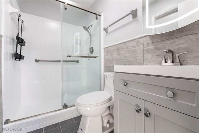 bathroom with tile walls, toilet, vanity, a shower stall, and tile patterned floors