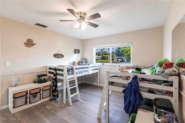 bedroom featuring a ceiling fan, visible vents, and wood finished floors