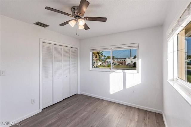 unfurnished bedroom featuring a closet, visible vents, a ceiling fan, wood finished floors, and baseboards