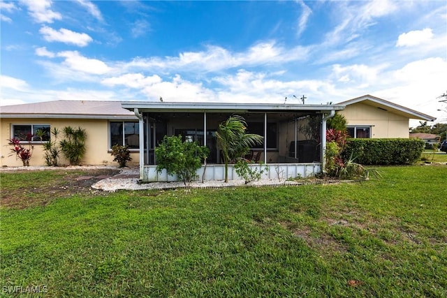 rear view of property with a sunroom, a lawn, and stucco siding