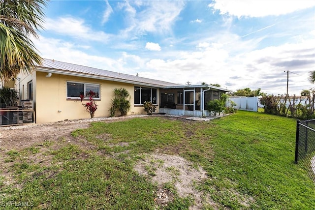 rear view of property featuring fence private yard, a sunroom, a lawn, and stucco siding