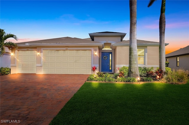 prairie-style house with a garage, a yard, decorative driveway, and stucco siding