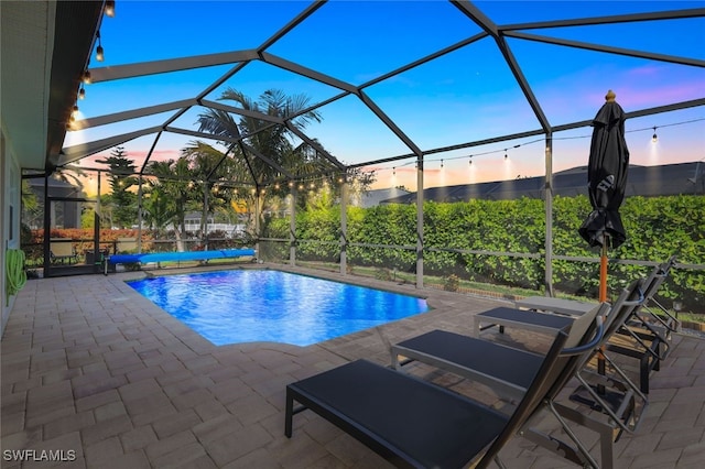 pool at dusk featuring glass enclosure, an outdoor pool, and a patio