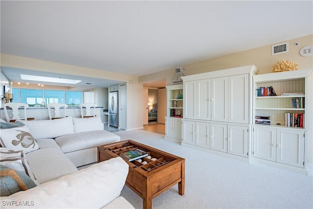 living area featuring a skylight, visible vents, and light colored carpet